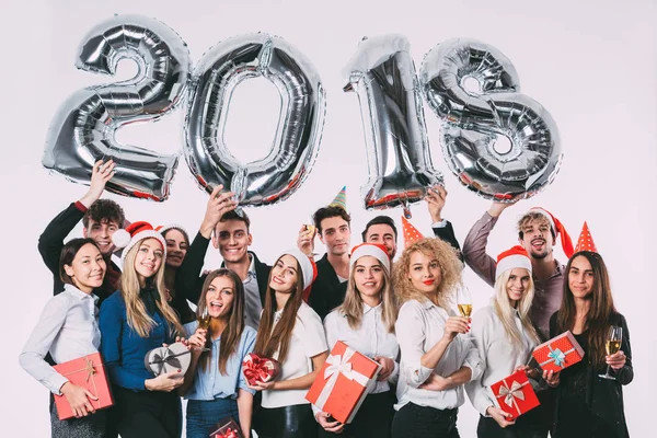 2018 nyår kommer! Grupp glada ungdomar i Santa hattar holding silver färgade antal ballonger. — Stockfoto