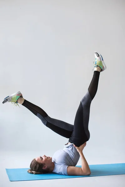 Jonge vrouw doet yoga of strekken op grijze achtergrond. — Stockfoto