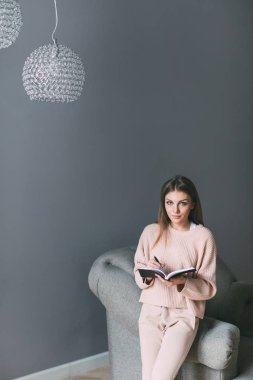 Ev sandalyede yakınındaki bir kitapla genç kadın.