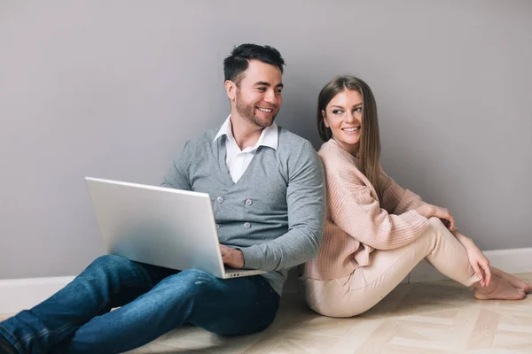 Hermosa pareja joven está utilizando un ordenador portátil y sonriendo mientras está sentado en el suelo . — Foto de Stock