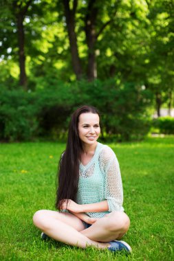 Çimenlerin üzerinde oturan genç gülümseyen kadın.