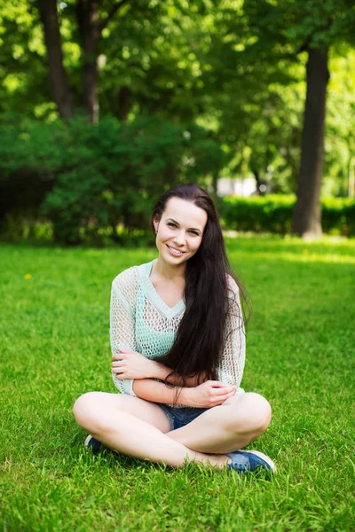 Sorrindo bela jovem mulher sentada na grama . — Fotografia de Stock