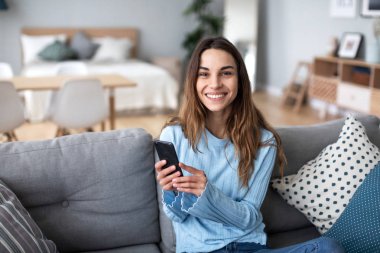 Mutlu, sıradan, güzel bir kadın cep telefonu kullanıyor. Evdeki koltukta oturuyor..