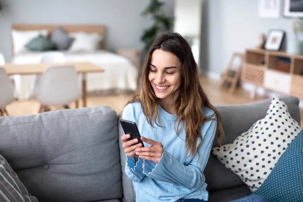 Joyeux jeune femme utilisant un téléphone portable tout en étant assis sur un canapé à la maison. — Photo