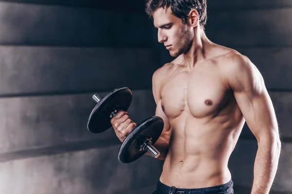 Guapo joven musculoso haciendo ejercicio con mancuernas . — Foto de Stock