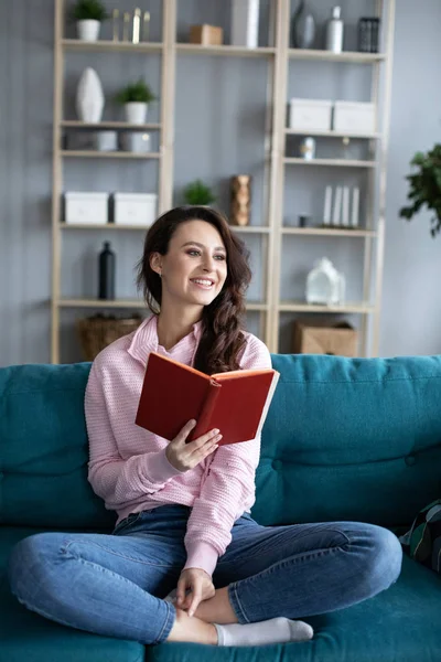 Jovem menina bonita aconchegante em um sofá lendo um livro . — Fotografia de Stock