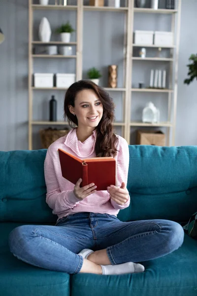 Jovem menina bonita aconchegante em um sofá lendo um livro . — Fotografia de Stock