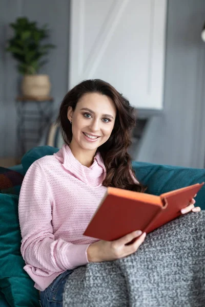 Femme heureuse avec un livre dans ses mains reposant sur un canapé confortable à h — Photo