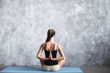 Koyu renk saçlı genç bir kadın spor paspası üzerinde elleri arkada oturuyor.