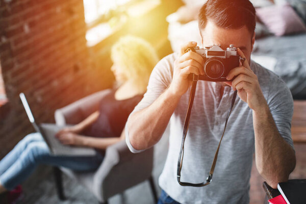 Фотограф фотографирует комнату, освещенную солнцем, на заднем плане сидит женщина. Человек с винтажной камерой
.