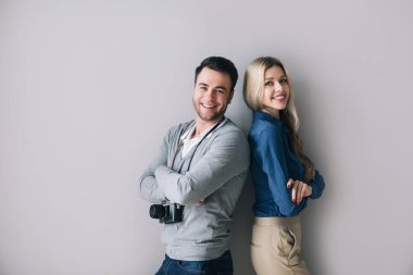 Kameralı yakışıklı bir adam ve gri duvarın yanında duran güzel bir kadın.