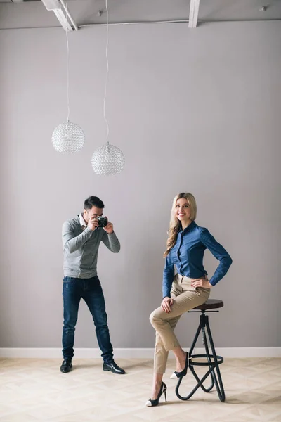 Odległe Zdjęcie Mężczyzny Fotografującego Ładną Kobietę Pokoju Szarymi Ścianami — Zdjęcie stockowe