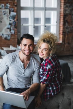 Evdeki kanepede dizüstü bilgisayar kullanan güzel bir çiftin portresi. Web sörfü.