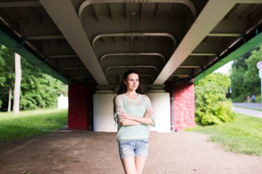 Köprünün altında elleri çapraz olan siyah saçlı bir kadın..