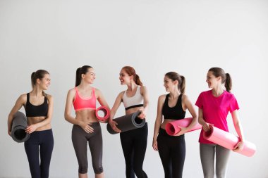 Yoga minderleri olan bir grup genç sportif kız tavan arası stüdyosunun beyaz iç kısmında duruyorlar. Spor salonunda kadın yoldaşlar fitness sonrası dinleniyor..