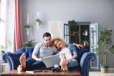 Çift, evdeki oturma odasındaki koltukta dizüstü bilgisayarlı bir geziyi araştırıyor. Seyahat planlıyorum..