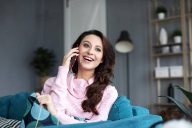 Güzel bir kadın evde telefonla konuşurken gülümsüyor ve yan tarafa bakıyor..