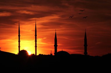 Gün batımında minaretler batar. Ramazan konsepti turuncu gökyüzündeki siluet camiler içindir..