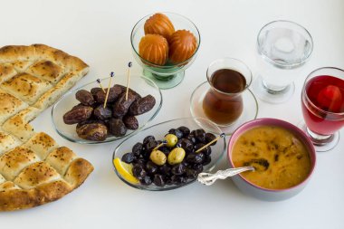 Ramazan 'ın sembolik gıdaları: ekmek, çorba, tatlı, hurma meyvesi, kırmızı gül şerbeti, zeytin, çay ve beyaz yüzeyde bir bardak su.