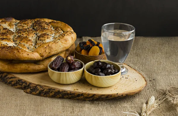 Iftar meal (time to break the fast) with sweet dry dates,apricot,black olives,water and Ramadan bread on the wooden board.Beginning meal before main menu.Close up taken.