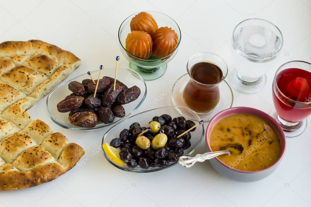 Symbolic foods of Ramadan:bread,soup,dessert,date fruits,red rose sherbet,olives,tea and a glass water on white surface.