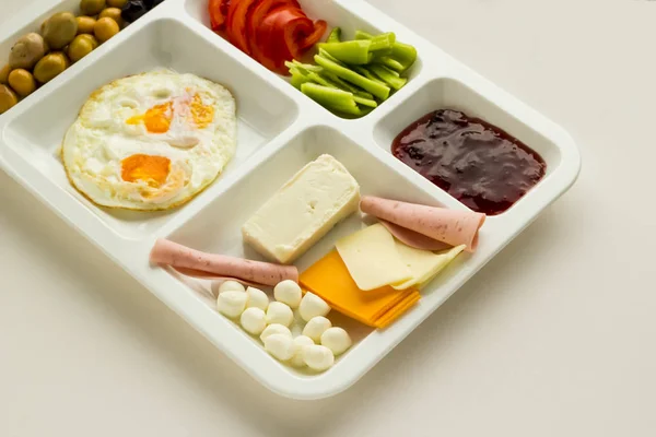 Egg, cheese, salami, olives, tomato, pepper and jam in a white hard plastic food tray (table d\'hote) on white background,tabldot name in TR.