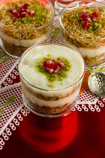 传统的 乳白色的 酥脆的斋月甜点奶油布丁 用烤过的Kadayif 石榴籽和切碎的开心果制成 图库照片