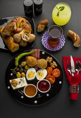 Siyah yüzeyde simit, köfte ve Türk Çayı ile büyük ve siyah tabaklar üzerine geleneksel Türk Kahvaltısı.