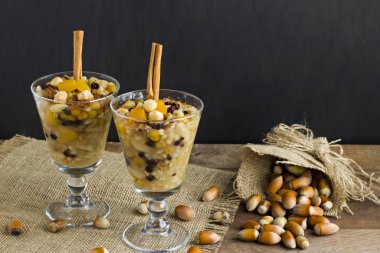 Geleneksel Tatlı Emin, Noah Pudding veya Ashura ahşap masada fındıklı şık bardaklarda tasarlandı. Emin Günü için kavramsal imge olarak kullanılan jüt peçete ve tarçın çubukları..