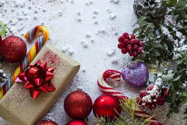 Beyaz yüzey üzerinde şeker kamışı, kırmızı toplar, hediye paketi ve kokina çiçeği (Kasap Süpürgesi) olan tebrik kartı gibi Noel veya yeni yıl tasarımı
