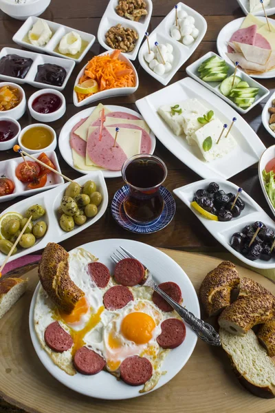 传统的土耳其撒播早餐在木桌上 鸡蛋在早餐桌前的白盘里放着香肠 垂直图像 — 图库照片