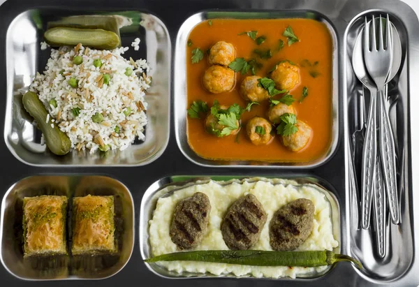 पारंपरिक तुर्की भोजन, मांसबॉल सूप, चावल, मसाले हुए आलू, ग्रिल किए गए मीटबॉल और स्टेनलेस स्टील खाद्य ट्रे में बक्लावा के दो टुकड़े। तालिका डी'होट "टीआर में ज्ञात टैबल्डोट" शीर्ष दृश्य स्टॉक तस्वीर