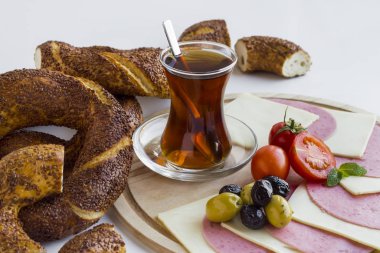 Susamlı simitlerin yakın plan çekimi, bir fincan Türk çayı, peynir, salam ve sebzeler beyaz üzerine