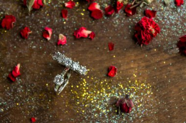 Tahta yüzeyde kırmızı kuru güllerle beş taş yüzük.