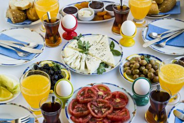 Dilimlenmiş domates, salatalık, peynir, tütsülenmiş hindi, zeytin, taze portakal suyu, çay ve haşlanmış yumurta ile yapılan zarif Avrupa kahvaltısı beyaz masa üzerinde dört servis..