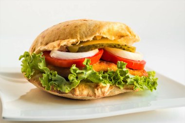 Domatesli kızarmış tavuk şnitzel burger, marul yaprağı, soğan ve beyaz arka planda salatalık dilimi..