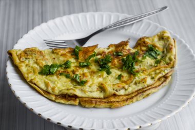 Beyaz yuvarlak porselen tabakta yarım omlet şeklinde katlanmış ve arka planda çatal var..