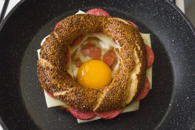 Kızartma tavasında susamlı, yumurtalı, peynirli ve salamlı sandviçin yakın plan çekimi.