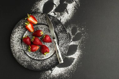 Yakın plan şeker tozlu lezzetli çilekler ve siyah yapraklar.