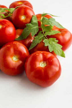 Beyaz yüzeyinde yeşil yaprakları olan taze, doğal domatesler. Üzerlerine su damlaları..