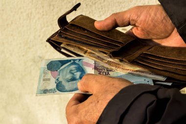 El, beyaz duvardaki kahverengi lider cüzdanından Türk 100 banknot çekmek. Yaklaş, izole edilmiş..