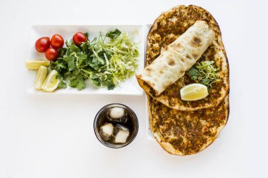 Geleneksel Türk Lahmacunu (Pizza) beyaz porselen tabakta, biri beyaz yüzeyde taze garnitürle sarılmış. Soğuk, köpüklü içecek. Yakından alındı, izole edildi..