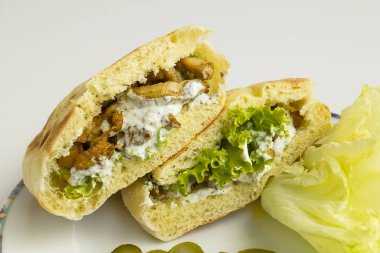 Donör, ekşi kremalı, domatesli, soğanlı ve marullu sandviç yap. Beyaz arkaplandaki Pita ekmeğine domates koy..