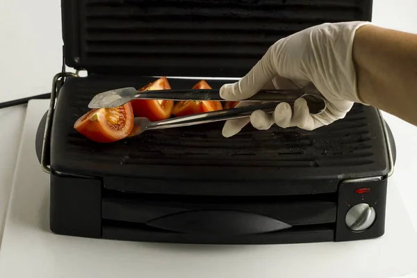 Hand Wearing White Gloves Cooking Tomato Metal Tongs Grill Machine — стоковое фото