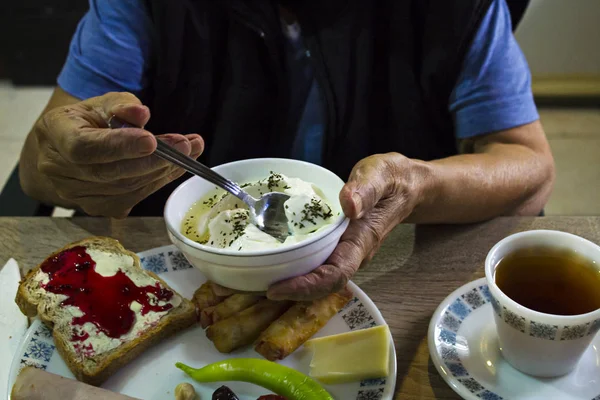 Old person hands holding bowl yogurt at the breakfast table.Close up taken.