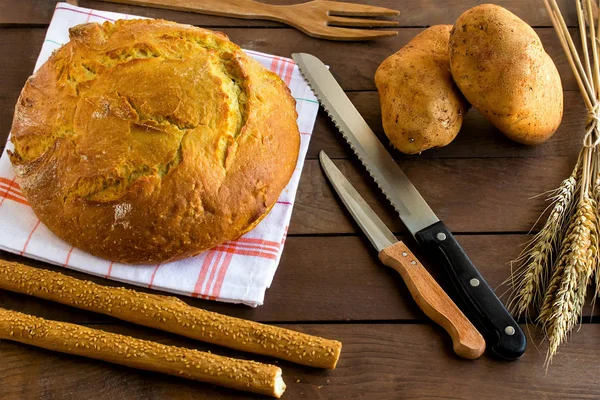 Traditional potato bread, two knives and potatoes on wooden table