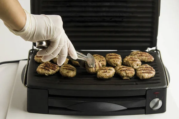 手戴白色手套 用黑色电炉煮肉丸子 白色背景 — 图库照片