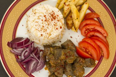 Geleneksel Türk bifteği karaciğer eti, siyah yüzeyde kızarmış patates, domates, soğan ve pirinç ile süslü tabakta dizayn edildi..