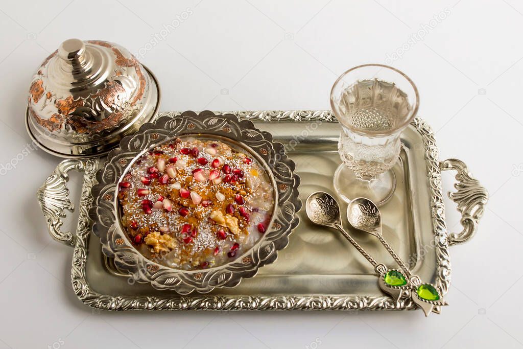 Traditional dessert Asure (Noah's Pudding) in a traditional silver bowl on silver tray with stylish,silver spoons and a glass of water.
