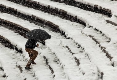 Şemsiyeli bir adam karlı merdivenlerden yukarı çıkar.